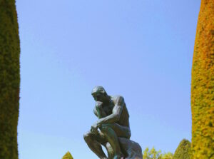 Escultura de bronze “O Pensador”, de Auguste Rodin, representando um homem nu sentado sobre uma rocha com a cabeça apoiada na mão, usada para ilustrar artigo sobre gatilhos mentais no plano de governo.