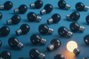 Fotografia ultra-realista em formato paisagem mostra dezenas de lâmpadas apagadas sobre um fundo em degradê azul, indo do azul claro ao azul cobalto. Entre elas, uma única lâmpada acesa em tom incandescente alaranjado se destaca, simbolizando criatividade no plano de governo.