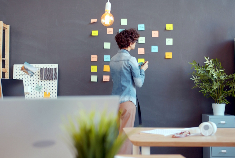 Pessoa organizando post-its coloridos em uma parede de lousa em um ambiente de trabalho moderno, simbolizando o processo de organização de ideias usado no Golden Circle no plano de governo.