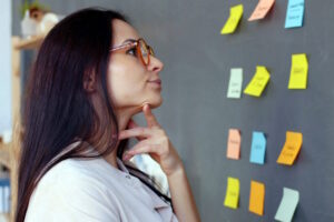 Mulher brasileira, candidata, em torno de 35 anos de idade, observa um painel com anotações enquanto reflete sobre decisões estratégicas; a cena representa as três perguntas que todo candidato precisa responder antes de elaborar um plano de governo consistente e bem posicionado.