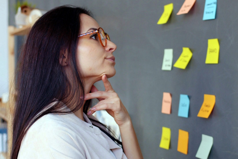 Mulher brasileira, candidata, em torno de 35 anos de idade, observa um painel com anotações enquanto reflete sobre decisões estratégicas; a cena representa as três perguntas que todo candidato precisa responder antes de elaborar um plano de governo consistente e bem posicionado.