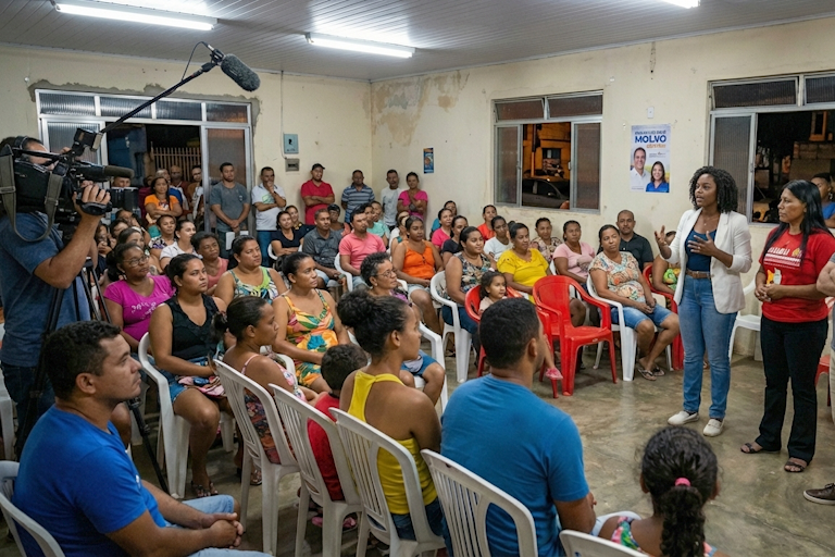 Reunião comunitária para elaboração do plano de governo com moradores sentados em cadeiras plásticas enquanto equipe registra em vídeo; plano de governo ajuda a construir a narrativa da campanha ao mostrar escuta popular e participação da comunidade.
