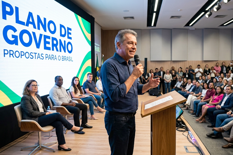 Candidato apresenta plano de governo em evento de lançamento para público em auditório, com telão exibindo propostas, ilustrando como fazer para que o plano de governo chegue a mais pessoas.